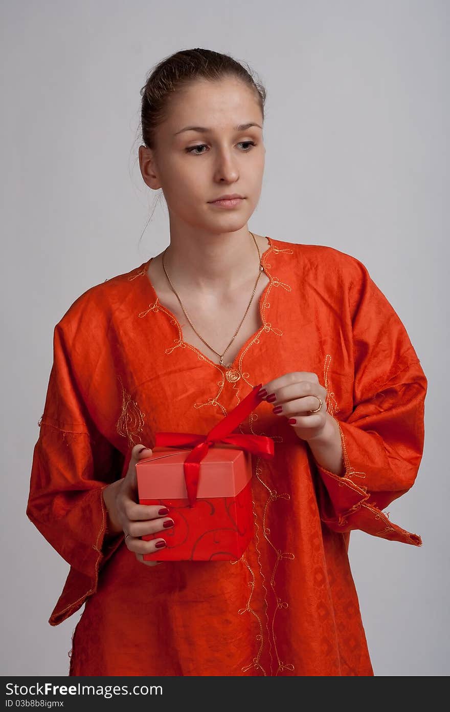 Thoughtful girl in an orange dress with a light background opens a gift. Thoughtful girl in an orange dress with a light background opens a gift