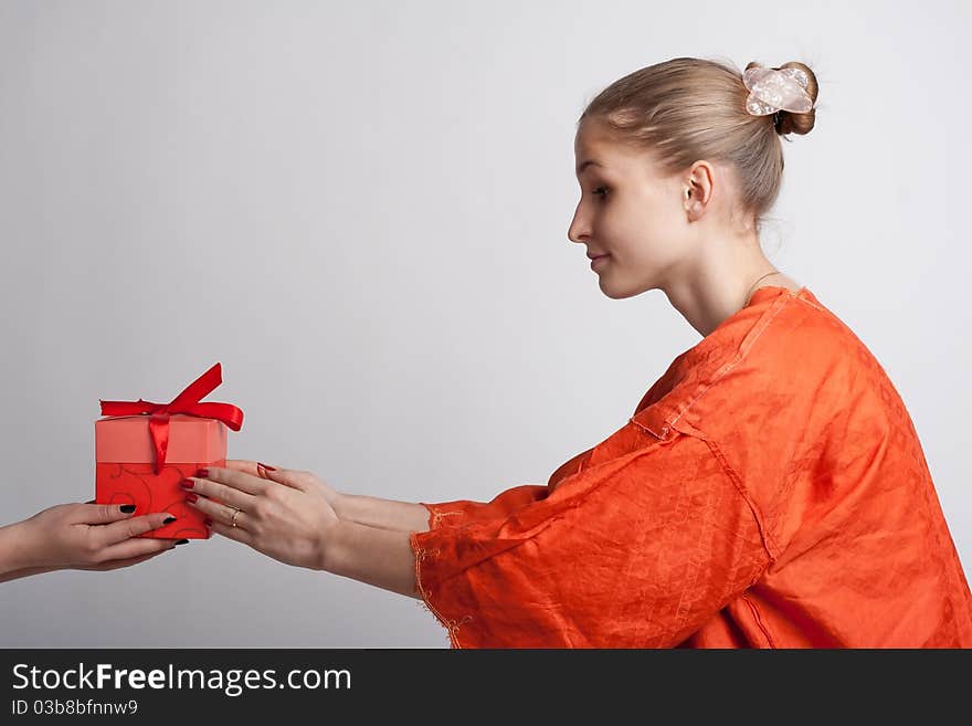 Girl in orange dress on a light background receives a gift. Girl in orange dress on a light background receives a gift