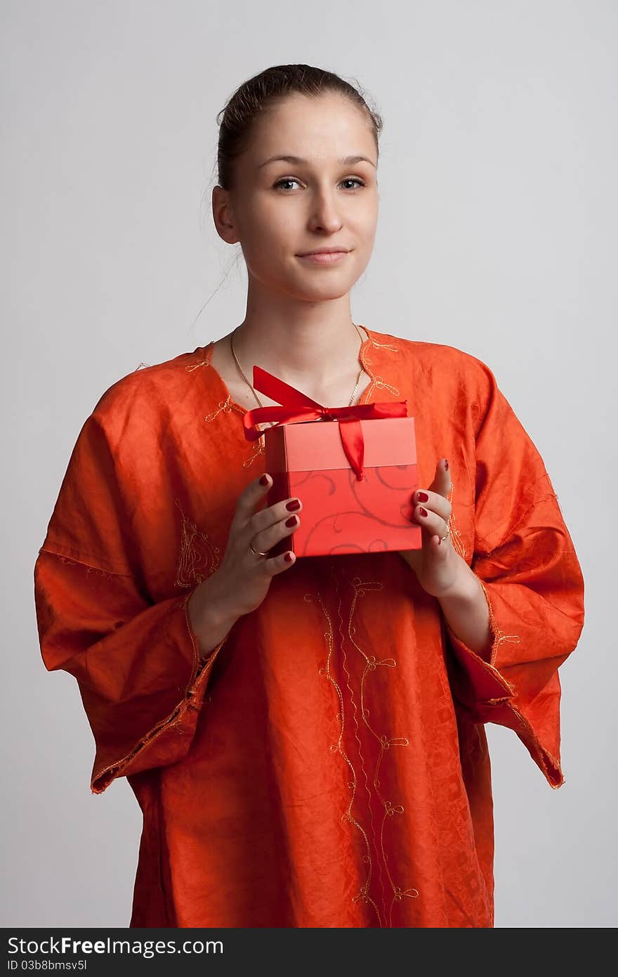 Girl in orange dress on a light background with a gift in the hands of. Girl in orange dress on a light background with a gift in the hands of