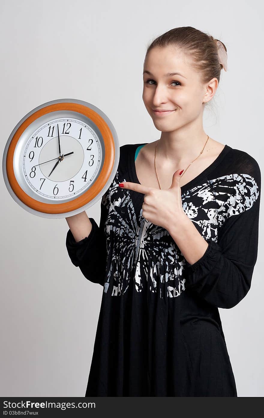 Beautiful girl on a white background shows the finger at the large clock in his hand which is almost noon. Beautiful girl on a white background shows the finger at the large clock in his hand which is almost noon