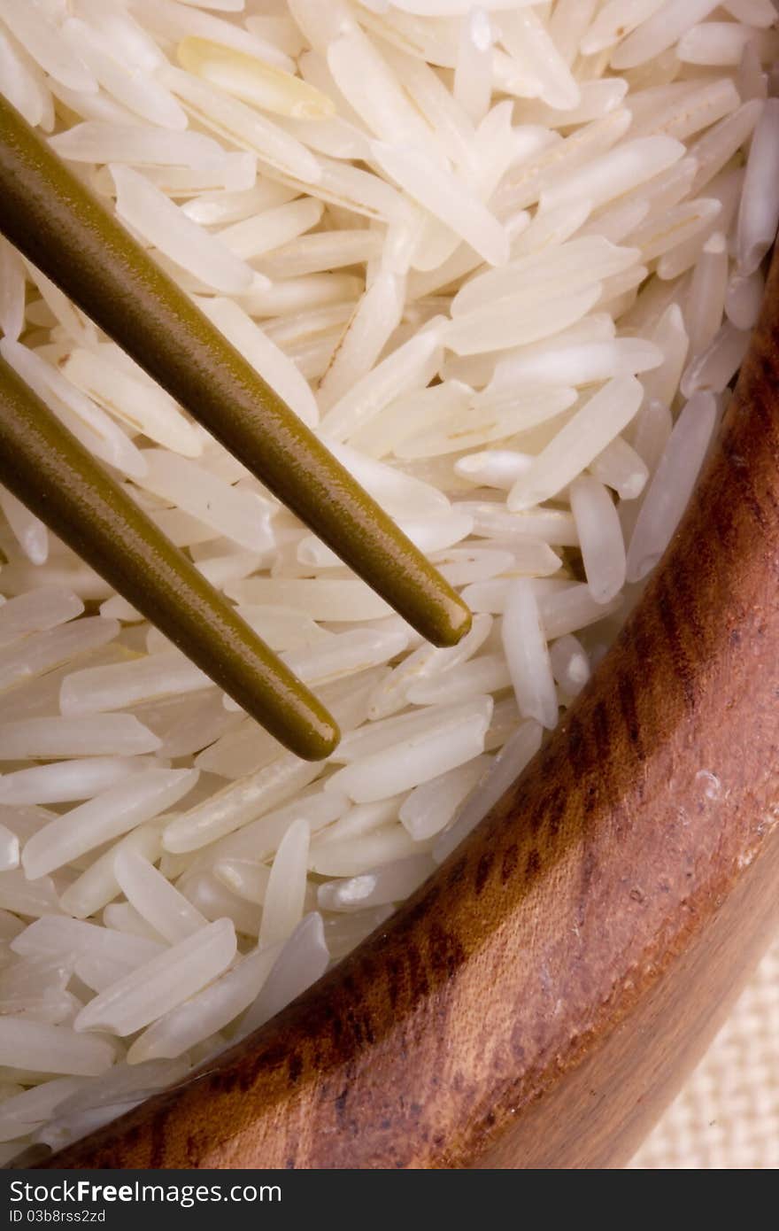 Close-up of white rice in a brown plate and golden chopsticks.