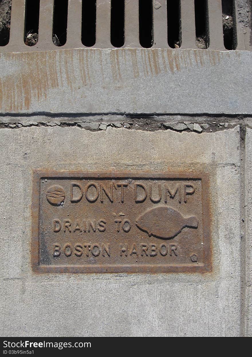 A metal sign cemented in concrete on Boston MA USA sidewalk next to storm drain. An environmental reminder to keep the harbor clean. A metal sign cemented in concrete on Boston MA USA sidewalk next to storm drain. An environmental reminder to keep the harbor clean