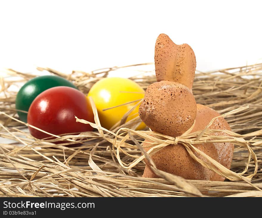 Easter Rabbit with three eggs in the background standing on straw. Easter Rabbit with three eggs in the background standing on straw