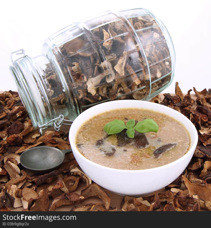 Mushroom soup in a bowl, decorated with basil, with dried mushrooms surrounding it and some in a jar, and an antique spoon. Mushroom soup in a bowl, decorated with basil, with dried mushrooms surrounding it and some in a jar, and an antique spoon