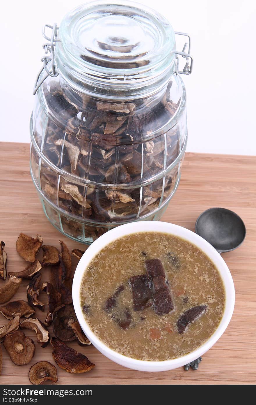 Mushroom soup in a bowl with dried mushrooms surrounding it and some in a jar, and an antique spoon. Mushroom soup in a bowl with dried mushrooms surrounding it and some in a jar, and an antique spoon