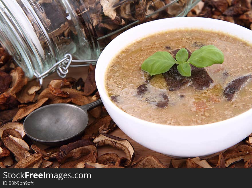 Mushroom soup in a bowl, decorated with basil, with dried mushrooms surrounding it and some in a jar, and an antique spoon. Mushroom soup in a bowl, decorated with basil, with dried mushrooms surrounding it and some in a jar, and an antique spoon