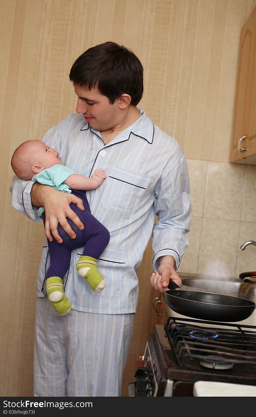 The young father with the baby on hands cooks food. The young father with the baby on hands cooks food