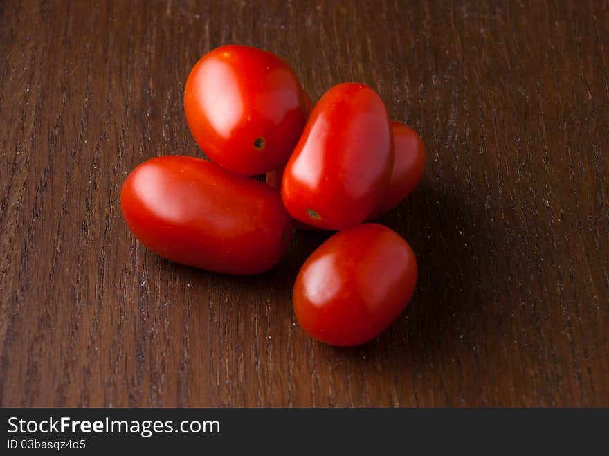 Five red cherry tomatoes stacked on a wood table. Five red cherry tomatoes stacked on a wood table.