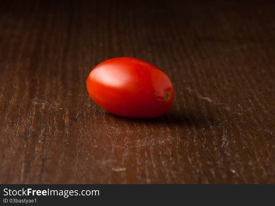 One single red cherry tomato on a wood table. One single red cherry tomato on a wood table