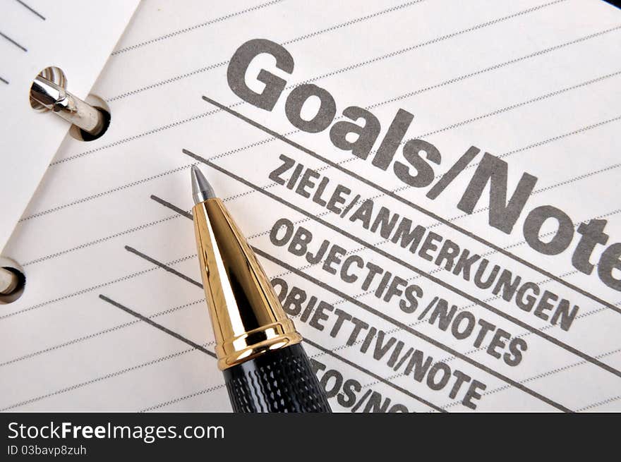 Goals plan or record in notepad and a ball pen, shown as woking on working goals, target, focus, objective important notes and other related business concept. Goals plan or record in notepad and a ball pen, shown as woking on working goals, target, focus, objective important notes and other related business concept.