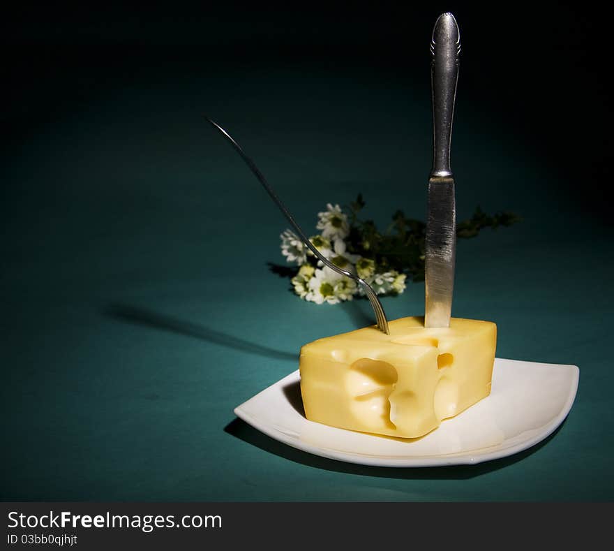 Knife and fork stick in cheese on cyan background. Knife and fork stick in cheese on cyan background