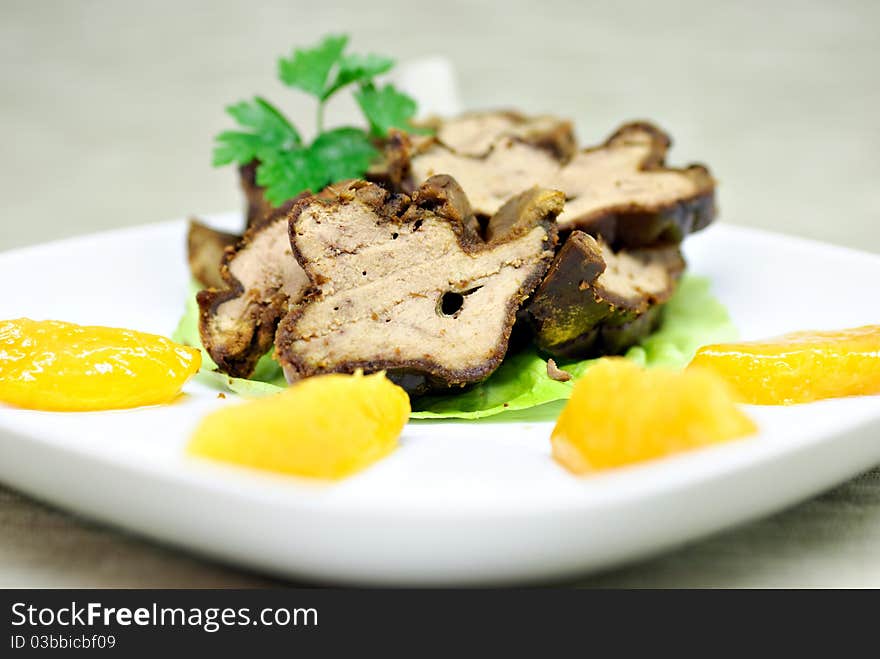 Roasted duck liver with peach on white plate.