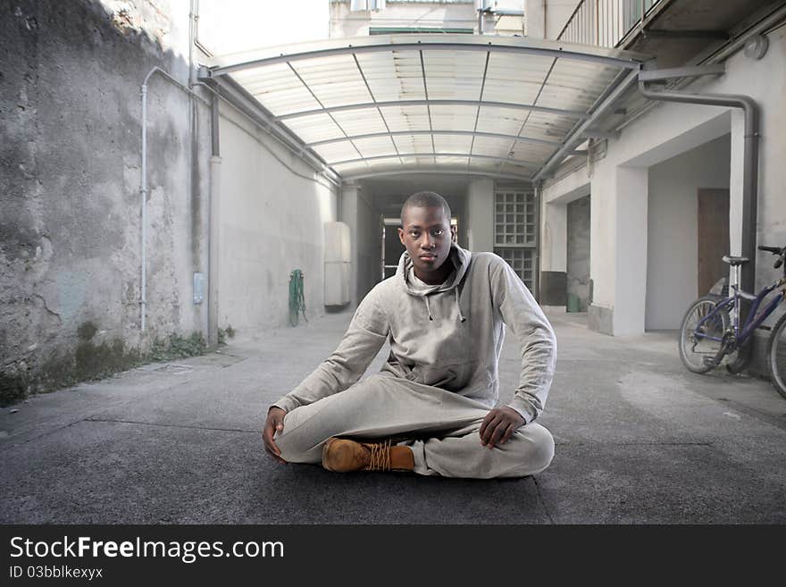 Young african man sitting on a street in front of a block of flats. Young african man sitting on a street in front of a block of flats