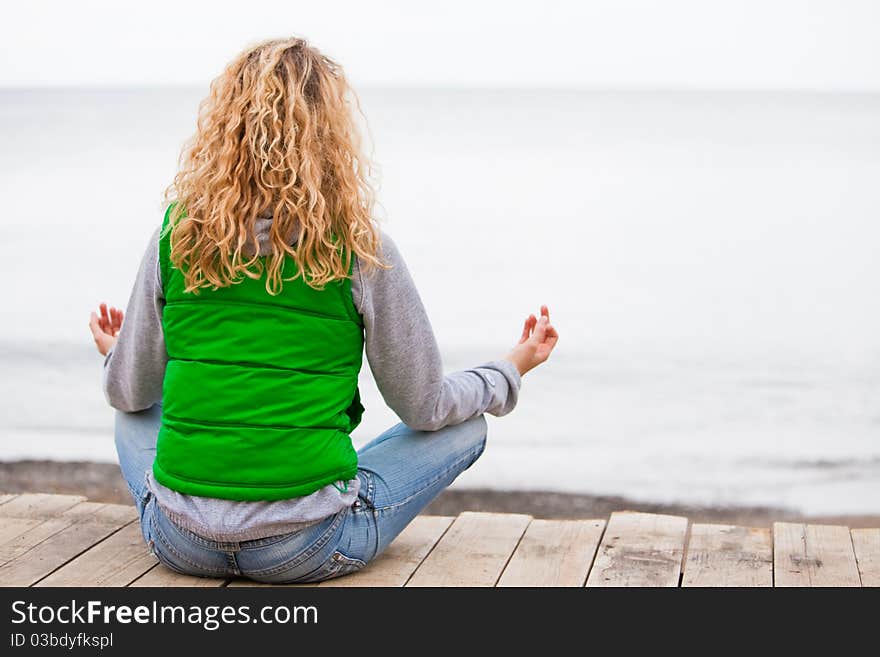 Yoga woman sitting on wooden bridge near the ocean