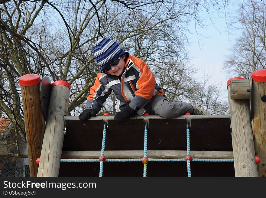 Young smiling boy getting over a barrier, having fun on a playground. Young smiling boy getting over a barrier, having fun on a playground