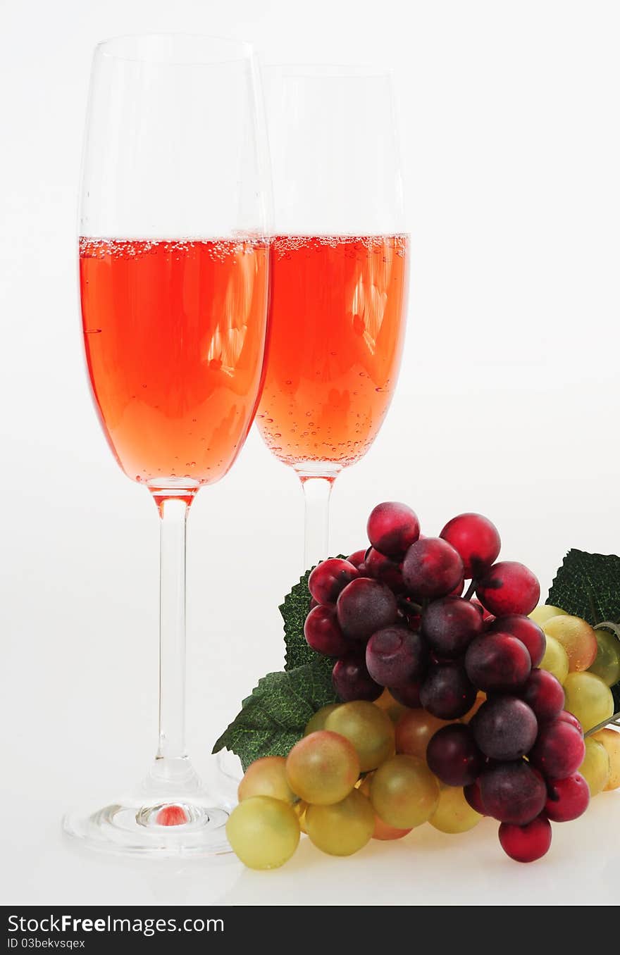 Two glasses of pink champagne on a white background, a branch of white and black grapes