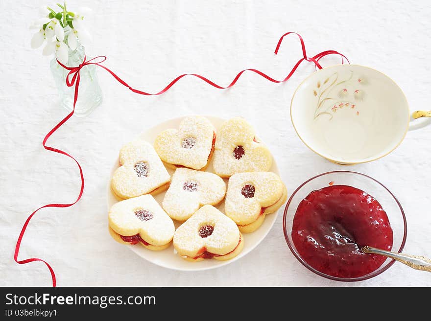 Biscuits in the form of hearts, strawberry jam in the cups, a bunch of snowdrops, a beautiful cup. Biscuits in the form of hearts, strawberry jam in the cups, a bunch of snowdrops, a beautiful cup