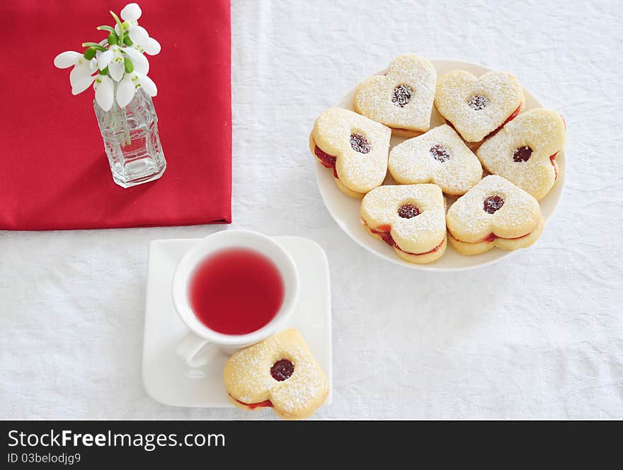 Fruit tea in a white cup cakes in the shape of hearts, red napkin and snowdrops. Fruit tea in a white cup cakes in the shape of hearts, red napkin and snowdrops