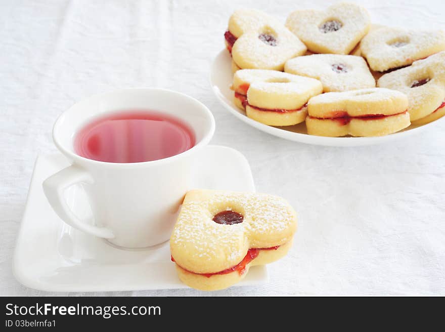 Fruit tea in a white cup and cookies in the shape of hearts on a white tablecloth. Fruit tea in a white cup and cookies in the shape of hearts on a white tablecloth