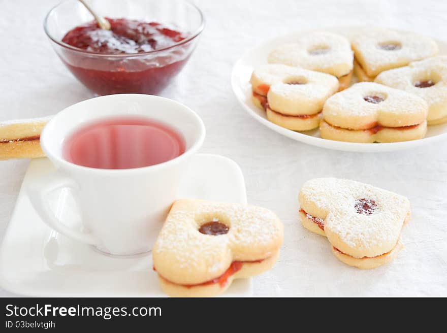 Fruit tea in a white cup, jam piala and cookies in the shape of hearts on a white tablecloth. Fruit tea in a white cup, jam piala and cookies in the shape of hearts on a white tablecloth