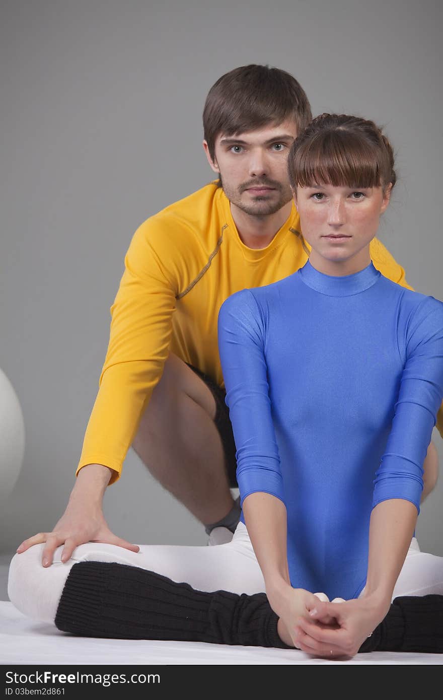 Woman in blue leotard and personal trainer helping to do stretching exercises. Woman in blue leotard and personal trainer helping to do stretching exercises