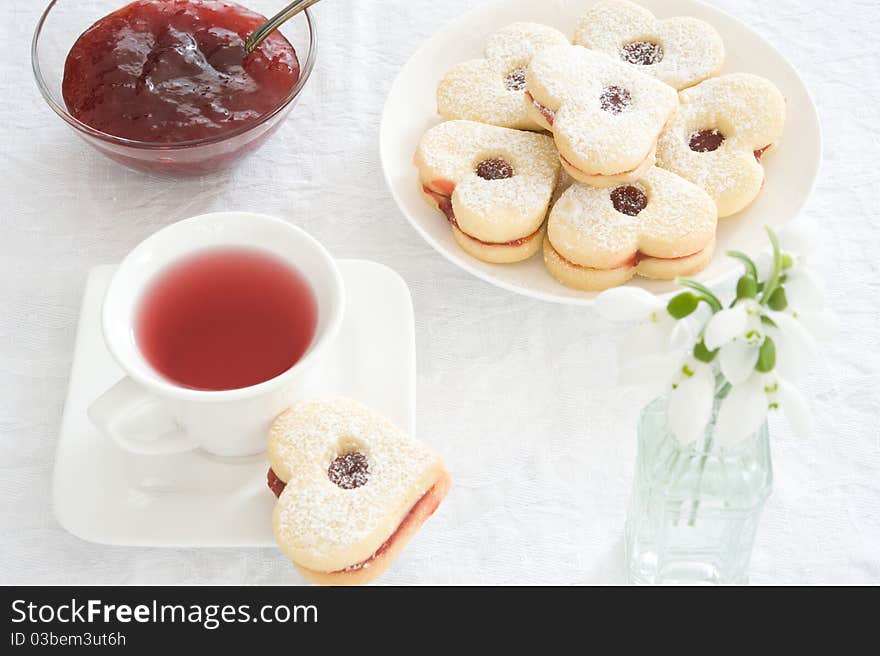 Fruit tea in a white cup, jam piala and cookies in the shape of hearts on a white tablecloth. Fruit tea in a white cup, jam piala and cookies in the shape of hearts on a white tablecloth