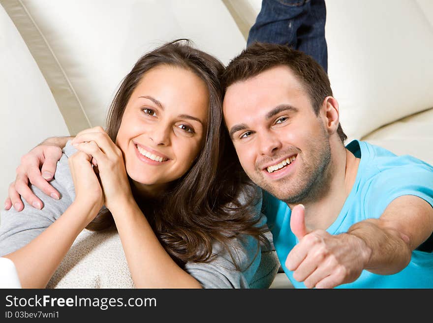 Young embracing couple on white sofa, boyfriend shows thumbnail. Young embracing couple on white sofa, boyfriend shows thumbnail