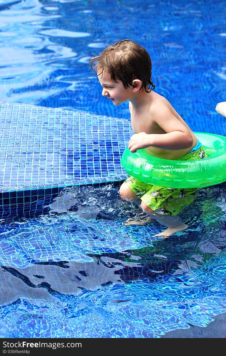 A white caucasian toddler boy about to jump from the steps into the blue tile pool with his green blown up inner-tube float. A white caucasian toddler boy about to jump from the steps into the blue tile pool with his green blown up inner-tube float.