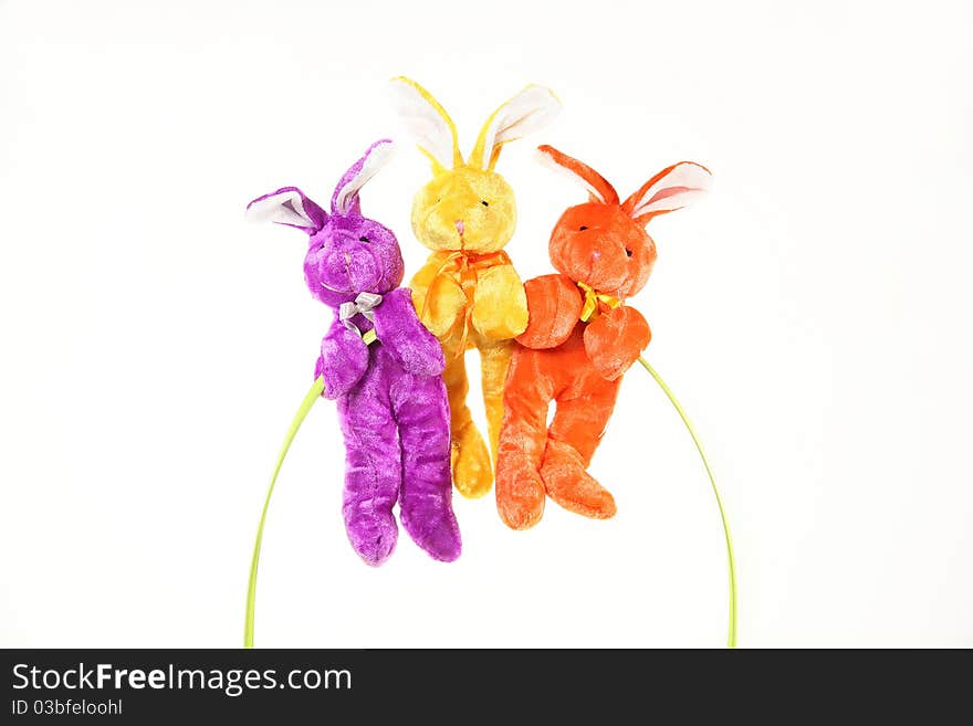 Three vibrant, colorful bunnies hang from handle of Easter basket with Sample text against white background. Three vibrant, colorful bunnies hang from handle of Easter basket with Sample text against white background.