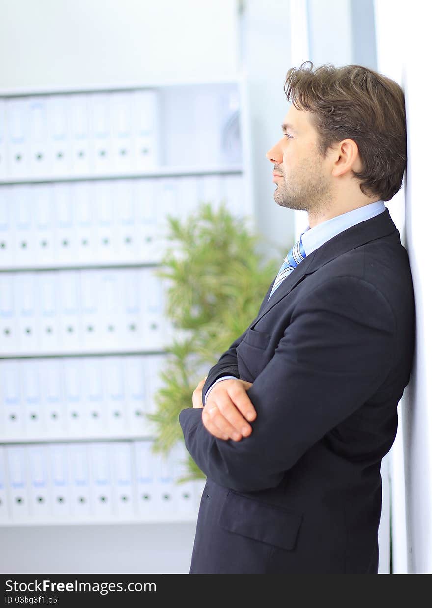 Young businessman standing in office lobby, using smartphone, smiling