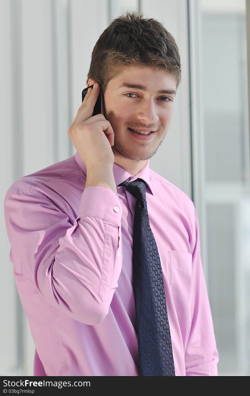 Young business man talk by cellphone over bright window in big hall