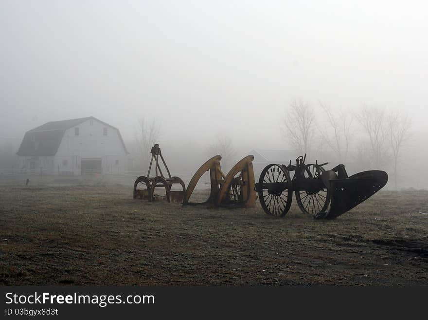 Old farm equipment and barn in foggy field. Old farm equipment and barn in foggy field