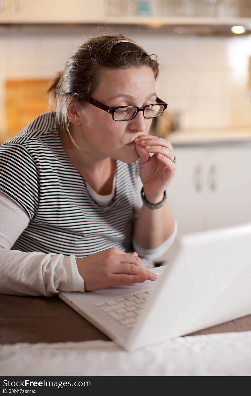 Woman sitting with her laptop in the kitchen with a worried expression. Woman sitting with her laptop in the kitchen with a worried expression