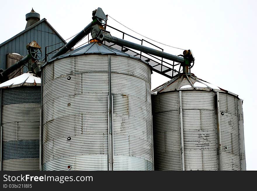 Grain storage bins in winter with an overcast sky. The overcast sky serves as a white background, helping with copy space. Grain storage bins in winter with an overcast sky. The overcast sky serves as a white background, helping with copy space.