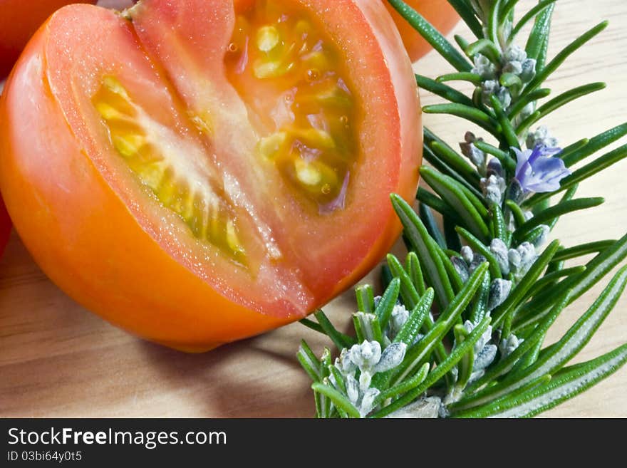 A close up of a tomato  sliced open on a wooden board with the herb rosemary. A close up of a tomato  sliced open on a wooden board with the herb rosemary