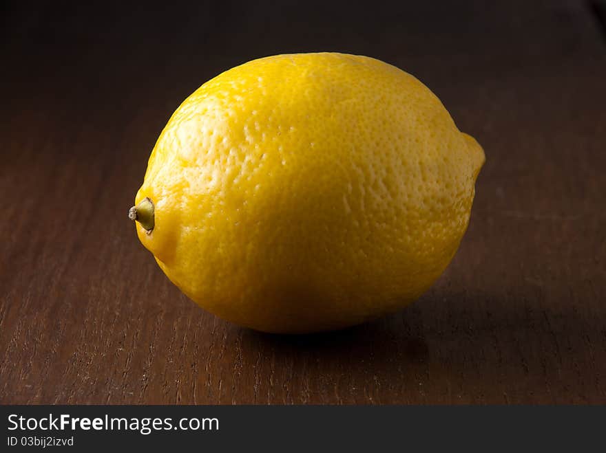 A single fresh yellow lemon on a wood grain table against a black background. A single fresh yellow lemon on a wood grain table against a black background.