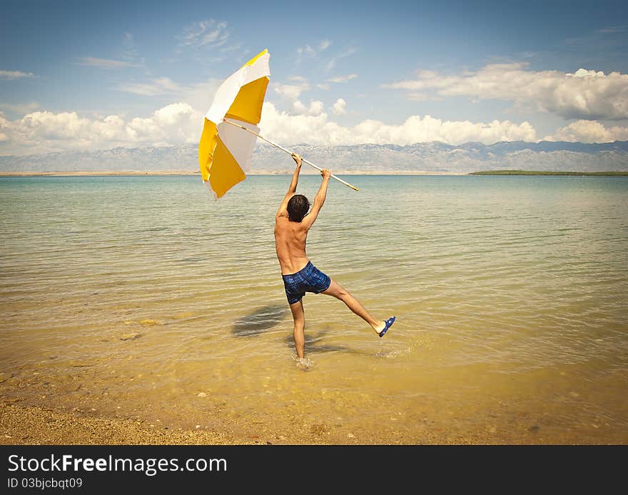 A happy young man on a beach holding a big open sun umbrella. A happy young man on a beach holding a big open sun umbrella