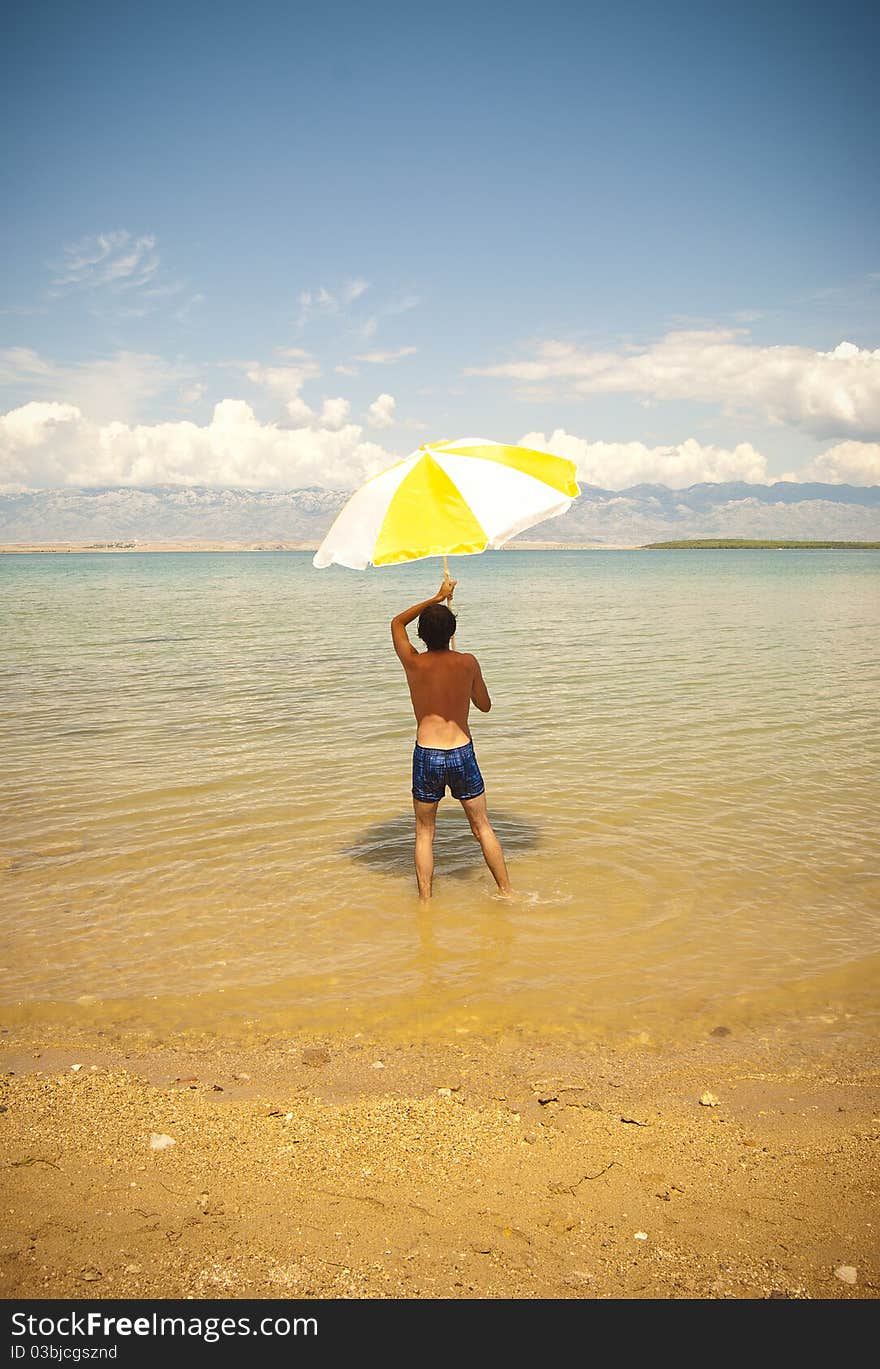 A young man on a beach holding a big open sun umbrella. A young man on a beach holding a big open sun umbrella