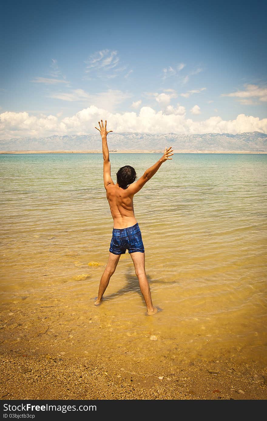 A young happy man stretching on a beach. A young happy man stretching on a beach