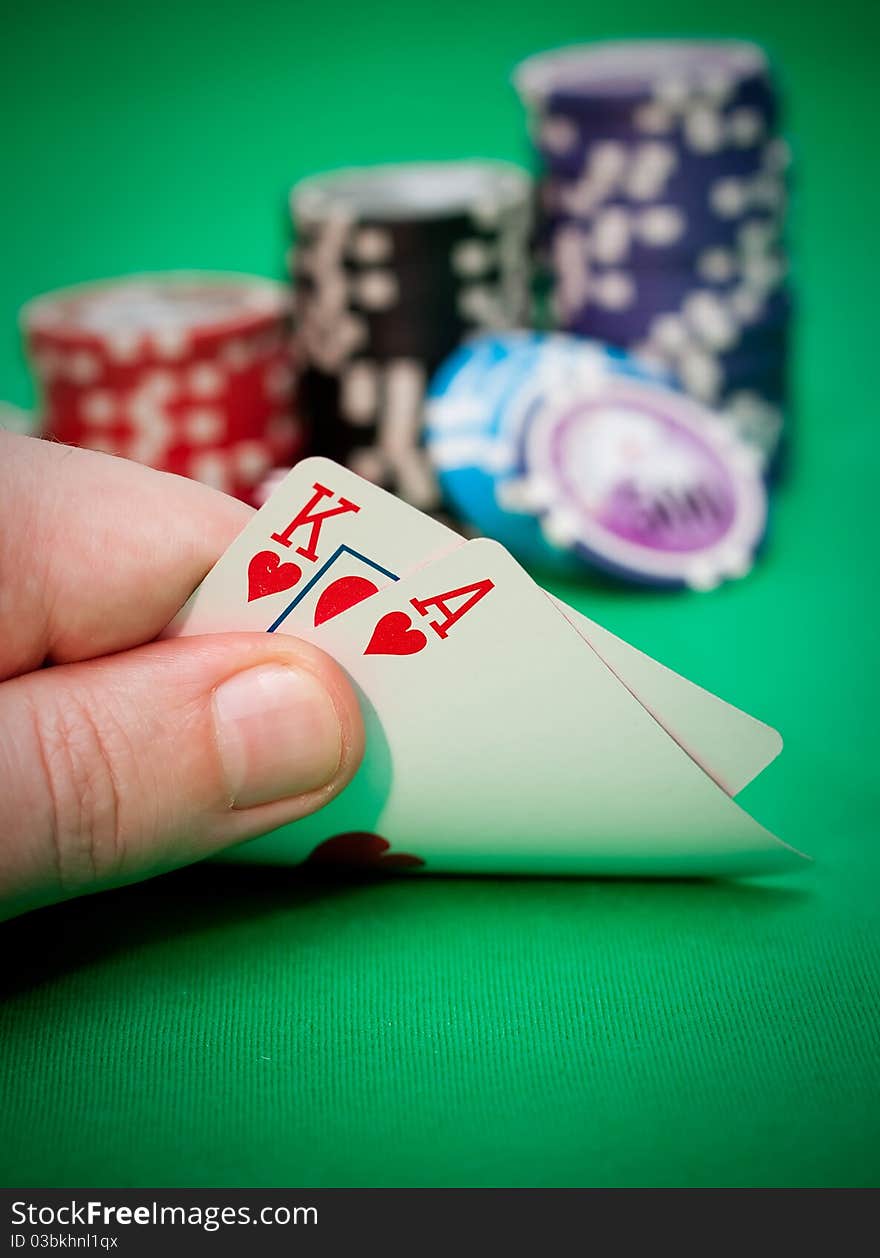 Poker chips and a hand flip the cards against green felt