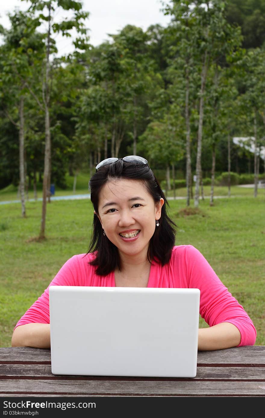 An Asian woman using her laptop at a park. An Asian woman using her laptop at a park