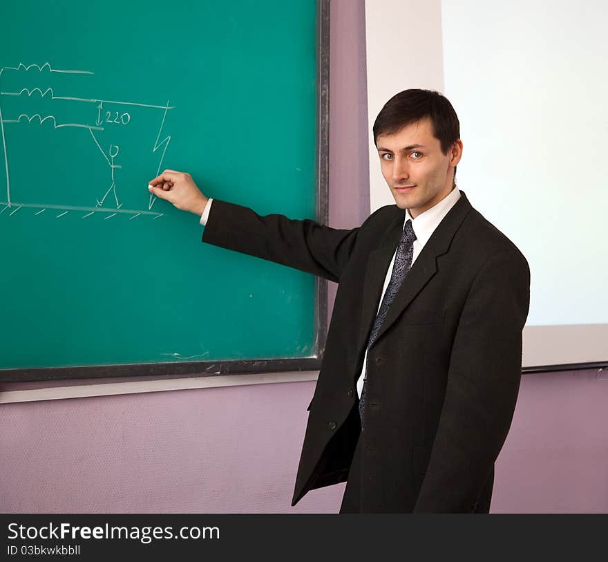 Young scientist giving a lecture on the background of the chalkboard with the scheme.