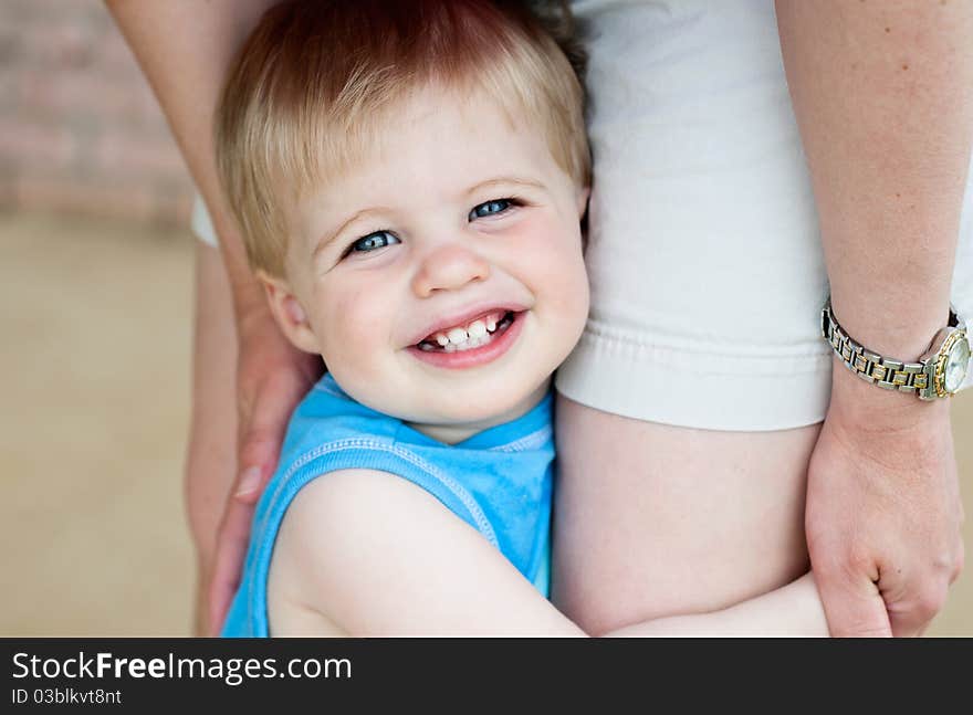 A cute little boy holding on to his Mother's legs, closeup with selective focus on face. A cute little boy holding on to his Mother's legs, closeup with selective focus on face