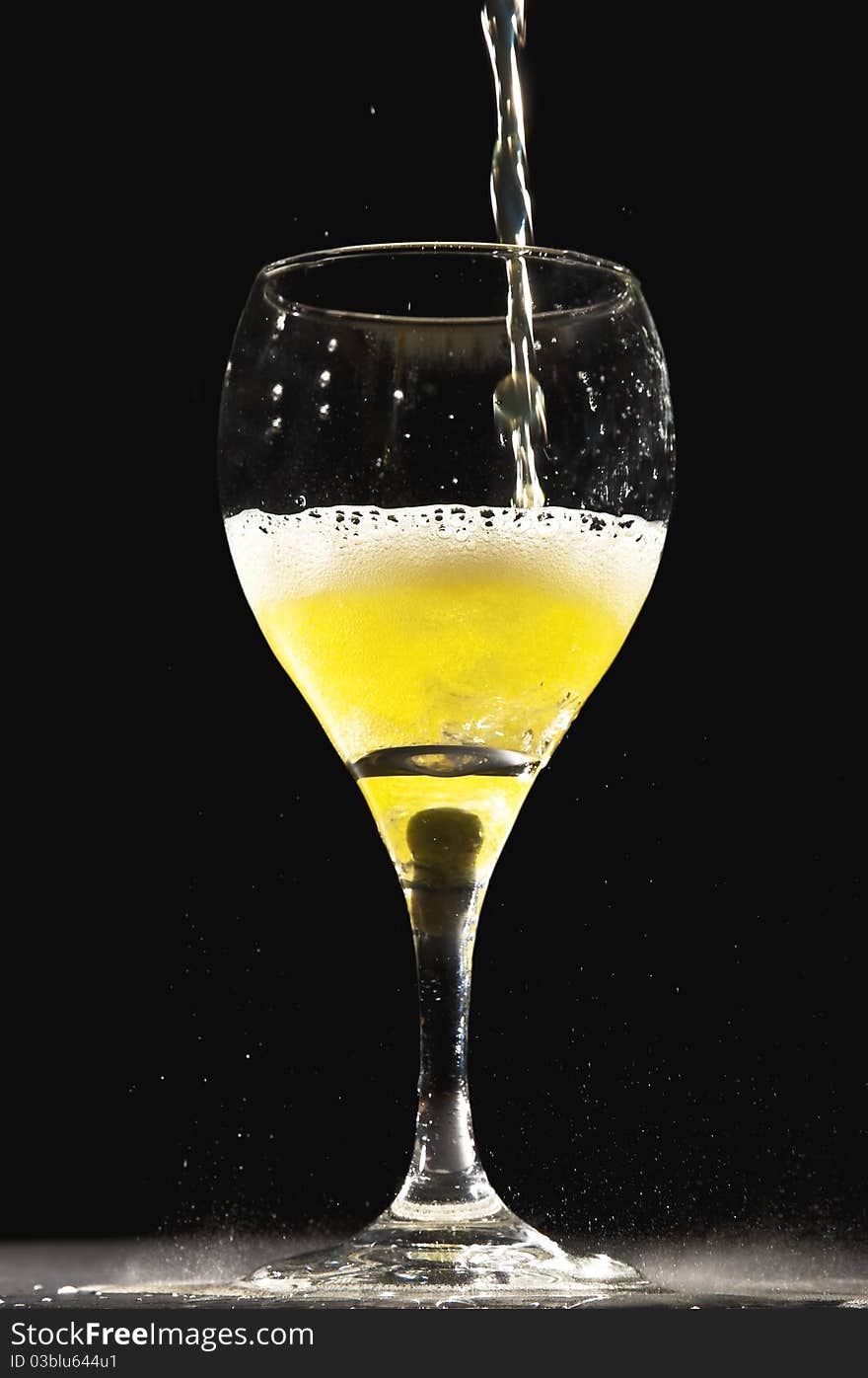 Yellow fizzling clear liquid being poured into champagne glass with a black background. . Yellow fizzling clear liquid being poured into champagne glass with a black background.