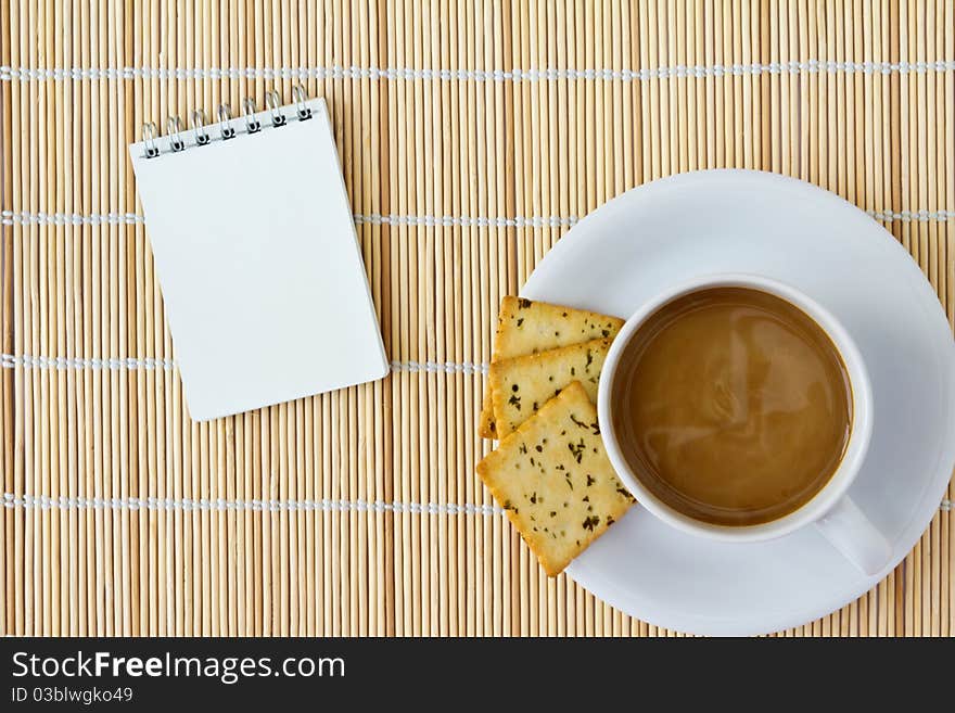 White cup of hot coffee and white sketch book on a mat