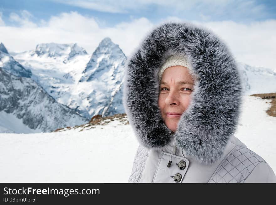 The elderly woman in a warm jacket with a fur collar travels in the winter in mountains. The elderly woman in a warm jacket with a fur collar travels in the winter in mountains.