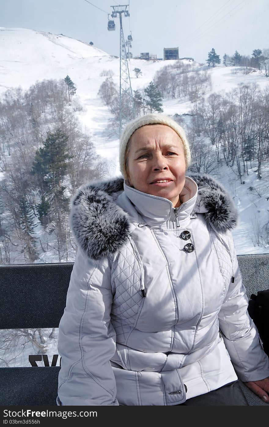 The elderly woman in a warm jacket with a fur collar rises upwards on a rope-way.