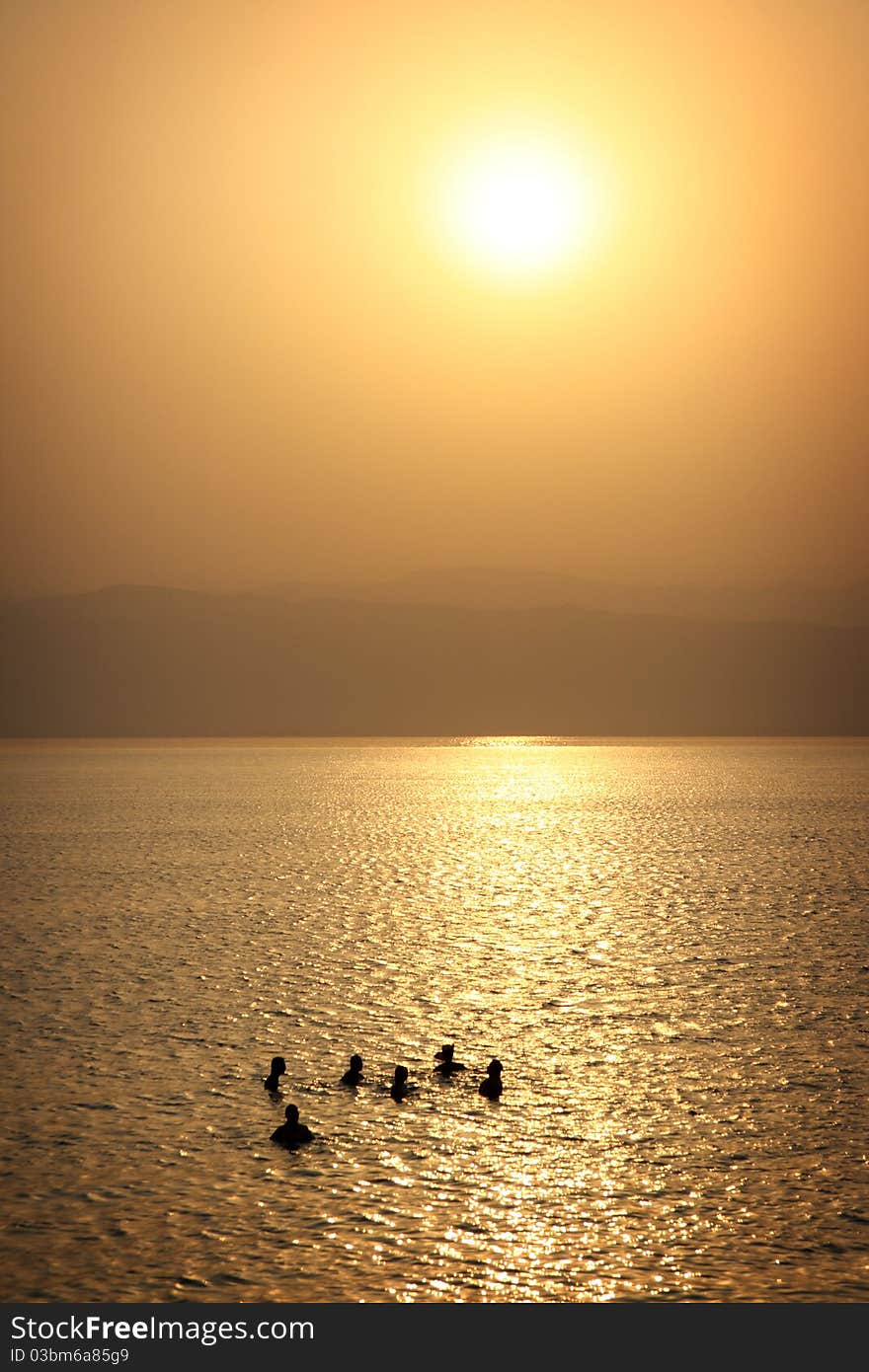 Tourists are enjoying the salty water of Dead Sea in a resort at the time of sunset. Coast of Israel on the background. Tourists are enjoying the salty water of Dead Sea in a resort at the time of sunset. Coast of Israel on the background.