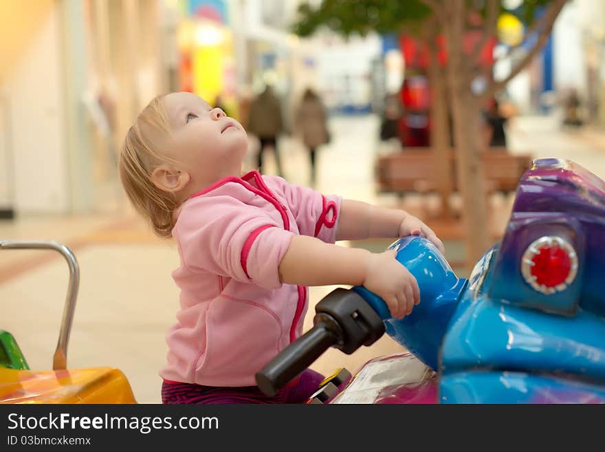 Young adorable baby ride on baby motorcycle in mall. Look up