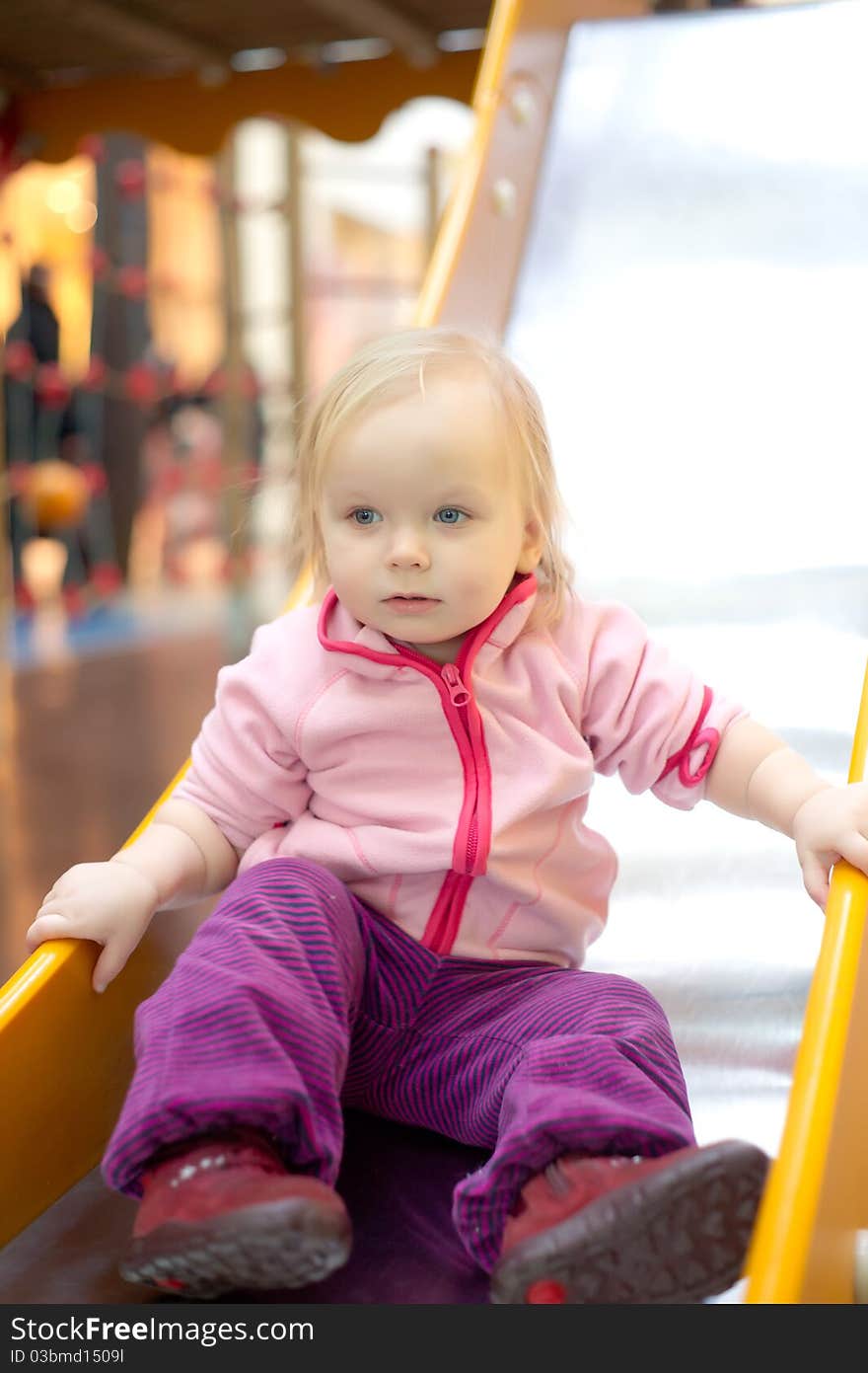 Young adorable baby sliding down baby slide on playground in mall. Sitting on the end of slide